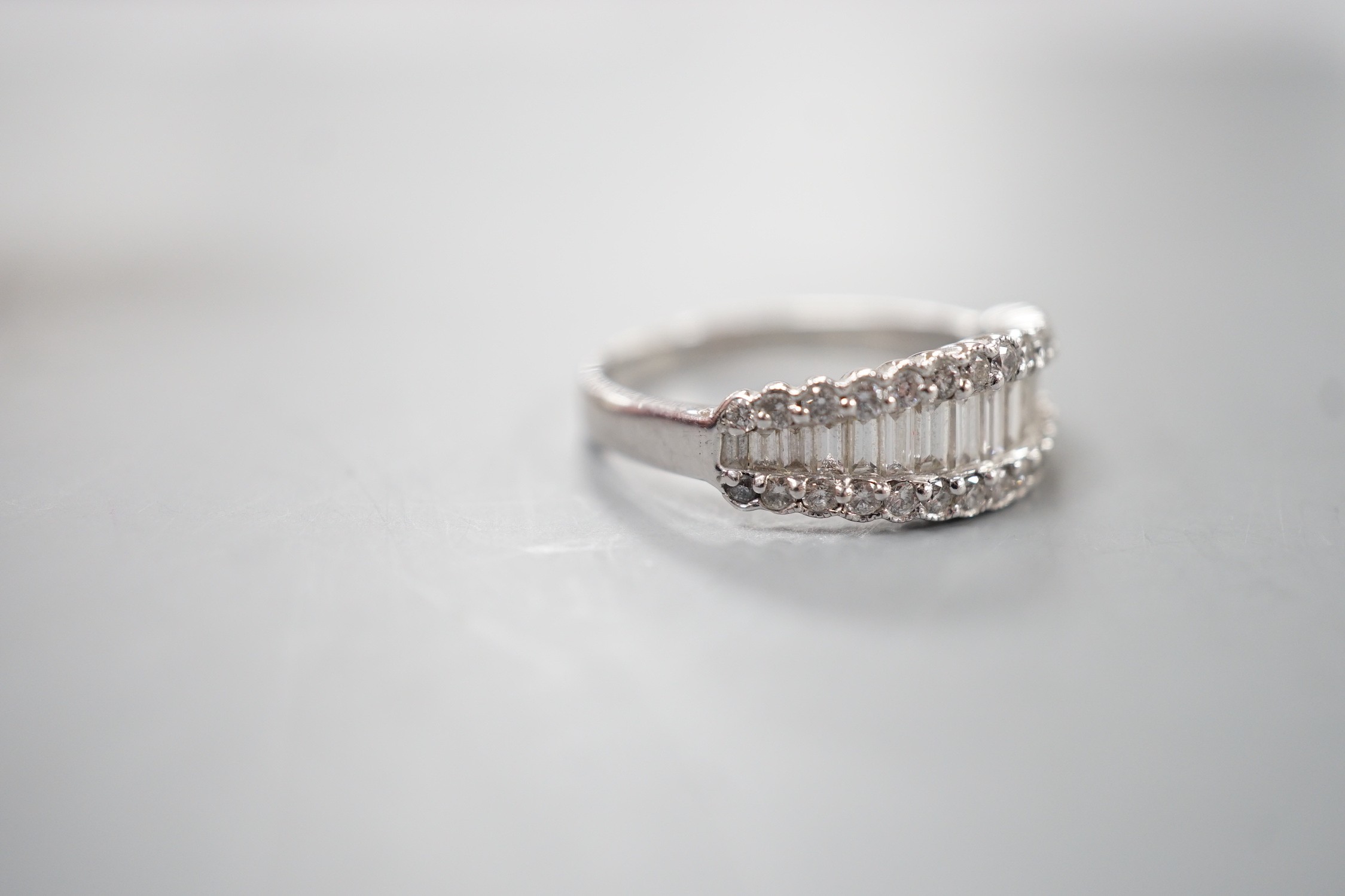 A modern white metal, graduated baguette cut diamond set half hoop ring, with diamond chip borders, size O, gross weight 5 grams.